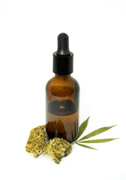 Бутылка с CBD маслом или настойка с листьями марихуаны и почки на белом фоне. CBD, препарат для медицинского использования, извлеченный из конопли. - Фото, изображение