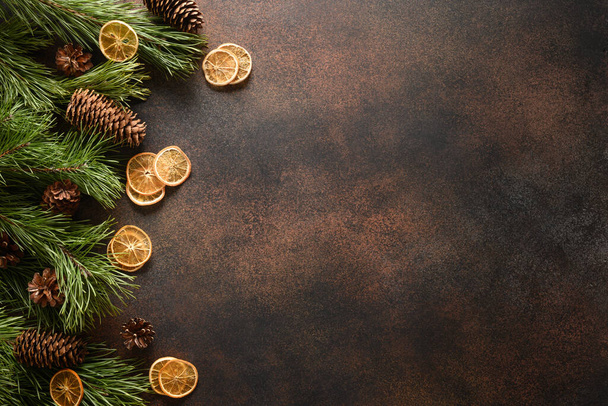 Christmas border with orange slice, aroma cinnamon, fir tree and cones on brown background. New Year. Top view. Xmas holiday greeting card. Copy space. - Foto, immagini