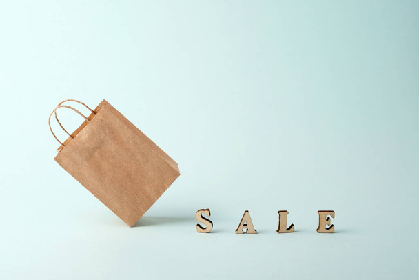 A paper shopping bag and the word sale on a blue background. The concept of delivery of purchases and sales. - Foto, afbeelding