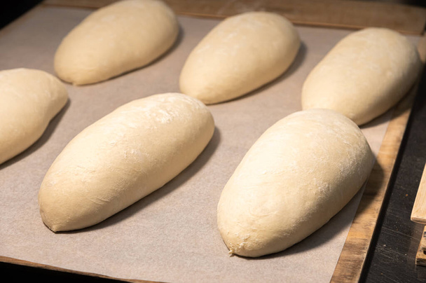 Several loaves of raw dough lie on a wooden board. Craft bread before baking - Photo, Image