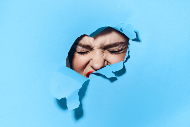 woman peeping through the holes in the poster blue studio background - Photo, image