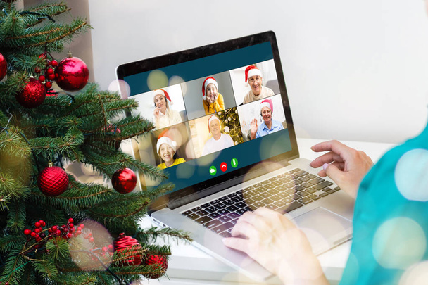 Saludos de Navidad en línea. una mujer con un suéter blanco y un sombrero rojo de Santa utiliza una computadora portátil para hacer videollamadas a amigos, padres y para ir de compras en línea - Foto, imagen