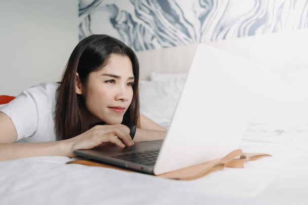 Woman works with laptop on the bed in concept of workation. - Zdjęcie, obraz