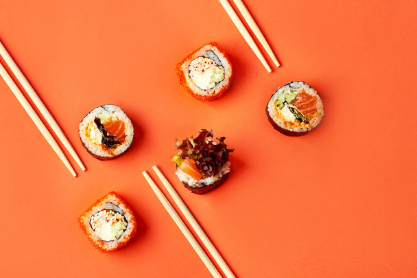 Různé druhy sushi rohlíků s tuňákem, úhořem, lososem. Mockup s chopsticki a sushi na oranžovém pozadí - Fotografie, Obrázek