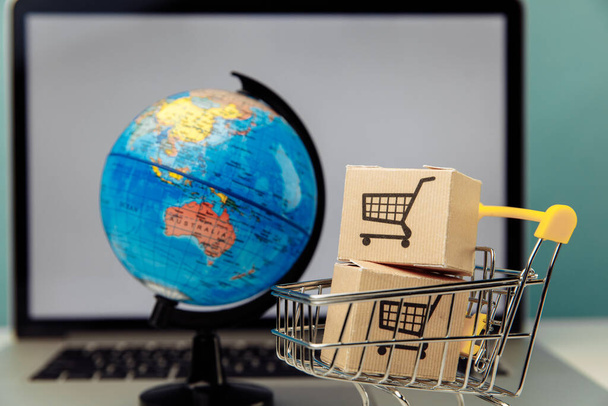 Compras en línea y concepto de comercio electrónico. Carro de compras Globe y supermercado con cajas en un fondo portátil - Foto, imagen