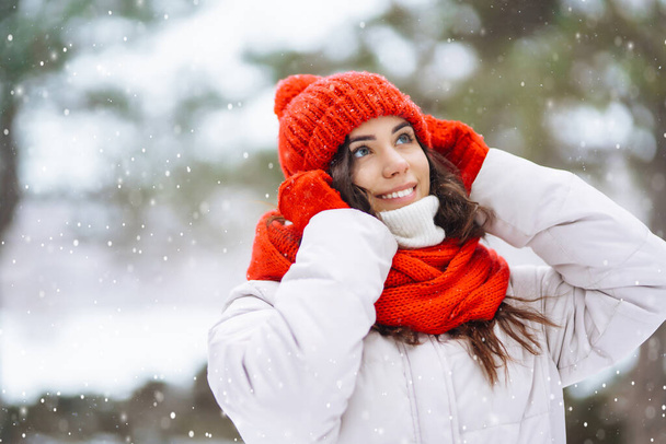 Winter smiling woman in red hat posing in a snowy park. Cold weather. Winter fashion, holidays, rest, travel concept. - Fotó, kép