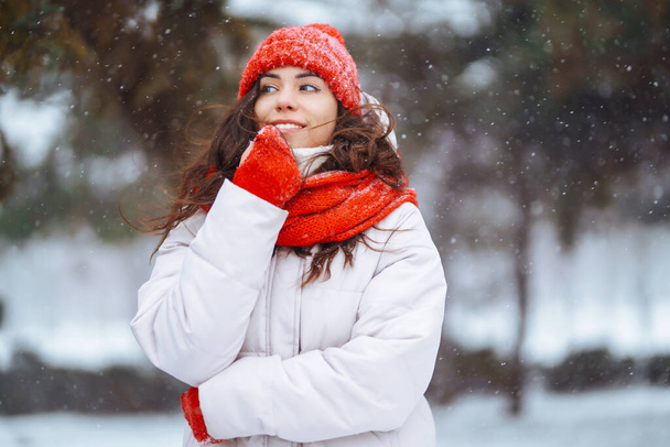 Winter smiling woman in red hat posing in a snowy park. Cold weather. Winter fashion, holidays, rest, travel concept. - Foto, afbeelding