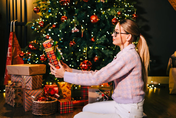Happy caucasian woman holding big Christmas present near Christmas tree. - Фото, зображення