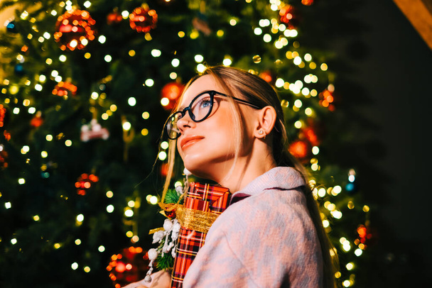 Happy caucasian woman holding big Christmas present near Christmas tree. - Φωτογραφία, εικόνα