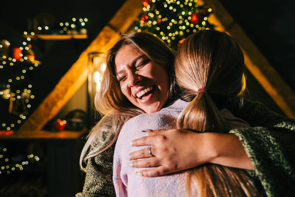 Christmas or new year celebration, two young happy woman embrace each other near christmas tree. - Фото, изображение