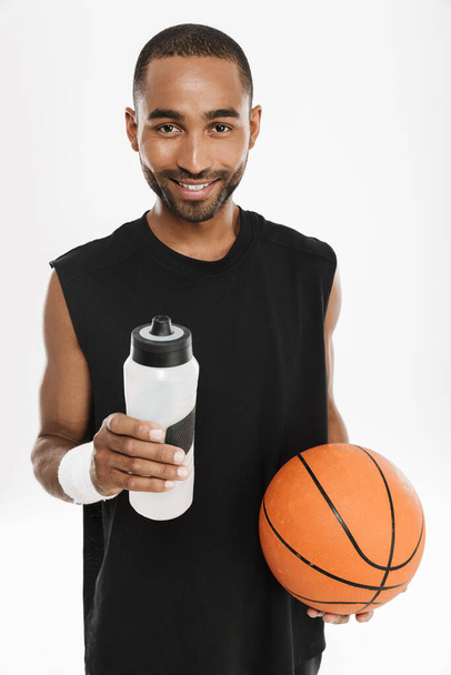 Young black sportsman drinking water while posing with basketball isolated over white background - Fotoğraf, Görsel