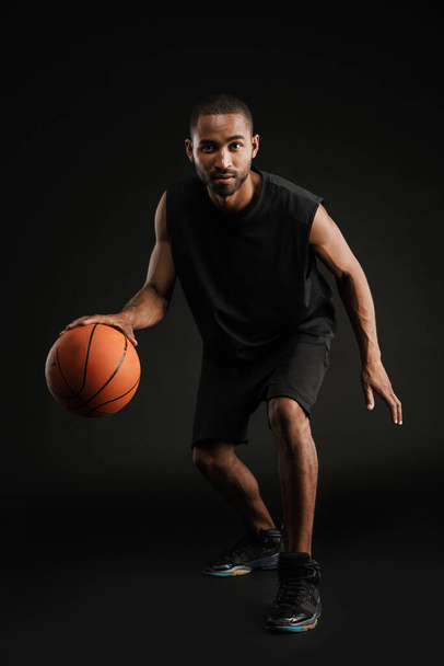 Young bristle sportsman playing basketball while working out isolated over black background - Фото, изображение