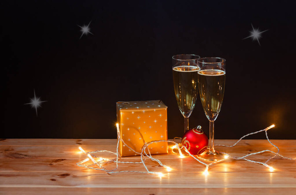 Vasos con champán, regalo de Navidad, bola y brillantes luces de Navidad sobre fondo oscuro. Ver con espacio de copia. - Foto, Imagen