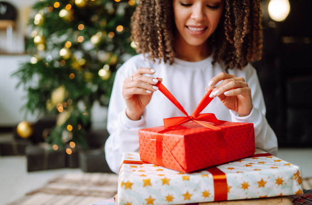 Christmas or New Year Gift in the woman hands. Young woman opens presents near the Christmas tree. Surprised. Winter holidays. - Фото, изображение