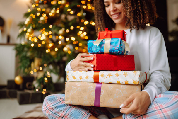 Christmas or New Year Gift in the woman hands. Young woman opens presents near the Christmas tree. Surprised. Winter holidays. - Foto, Imagem