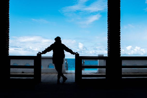 Bir deniz manzarasının arka planında bacak bacak üstüne atmış bir adamın silueti. İnsan ve deniz yapıları. gölge ve ışığın karşıtlığı - Fotoğraf, Görsel