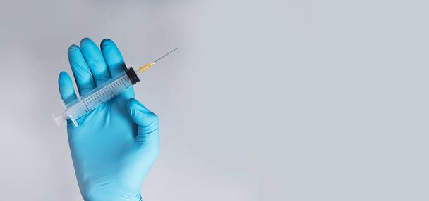 Clean syringe with sharp needle in doctors hands in glove on blue gray background. Banner with copy space for medical ad - Foto, immagini