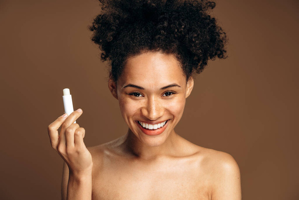 Lips protection. Beautiful woman with beauty face and curly hair preparing to applying lip balm at her lips. Portrait of female model with natural makeup. Lips skin care cosmetics concept - Foto, imagen