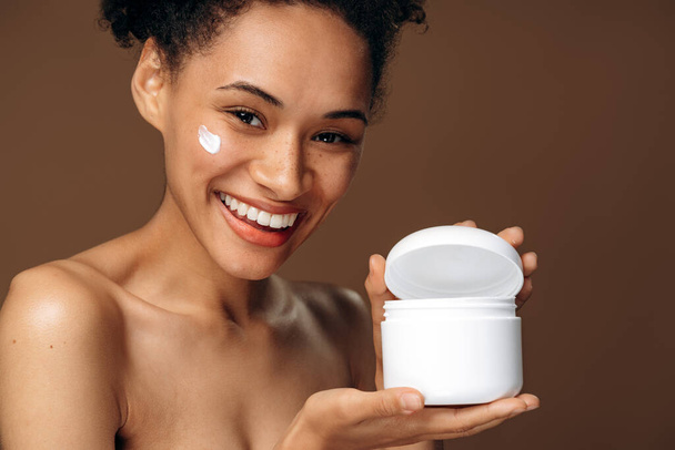 Woman posing to the camera with happy smile while holding the bottle with moisturizer. Happy woman taking care of her skin. Beauty concept - Φωτογραφία, εικόνα