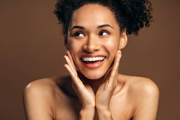 Natural beauty. Portrait of overjoyed multiracial brunette girl with perfect skin and nude makeup posing over brown studio background while looking away - 写真・画像