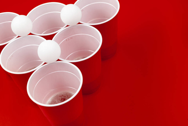 Cups and plastic ball on red background. Beer pong game - Foto, imagen