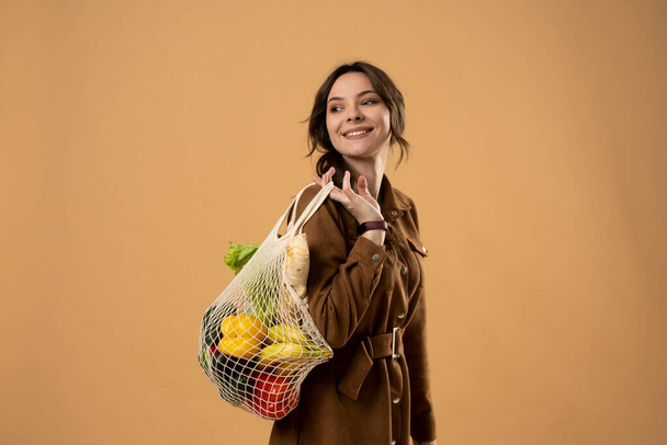 Koncept nulového odpadu. Mladá brunetka drží opakovaně použitelnou bavlněnou nákupní tašku s potravinami z trhu. Koncept bez plastu. Bez odpadu, bez plastu. Udržitelný životní styl. - Fotografie, Obrázek