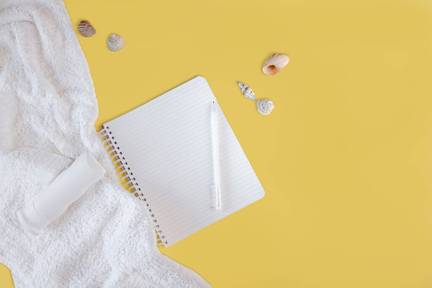 The concept of a summer vacation with a white towel and a tanning agent, with a white notebook, pen and shells on a yellow background. Vacation plans. Dreams. - Foto, Imagen