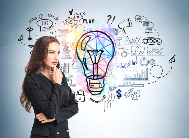 Attractive businesswoman is standing near colourful sketch with light bulb, cogwheel, plan, padlock security, dollar, pie and bar diagram on wall. Concept of imagination for creative idea - Foto, afbeelding