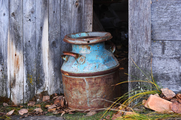 Das Bild einer verrosteten alten Milchkanne im Eingang einer alten, heruntergekommenen Scheune.  - Foto, Bild