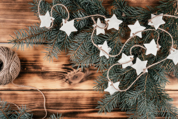 Étoiles de Noël maison guirlande de porcelaine froide avec des branches d'épinette sur fond de bois brûlé. Vue du dessus - Photo, image