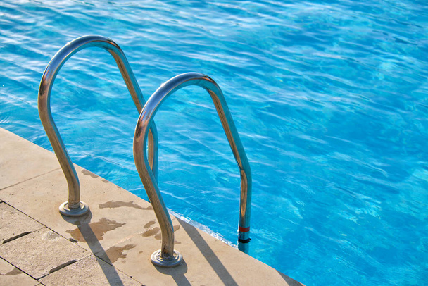 Close up of swimming pool stainless steel handrail descending into tortoise clear pool water. Accessibility of recreational activities concept. - Fotó, kép