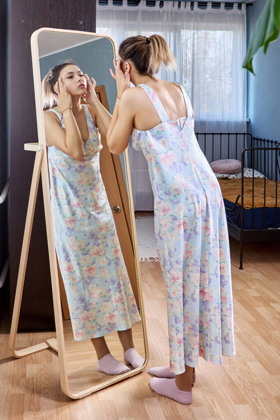Large full length standing mirror and woman in dress is looking in it. - Fotó, kép