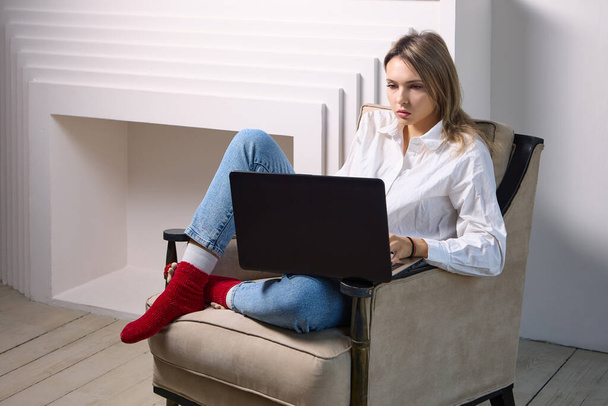Woman with laptop sits in armchair in lounge interior. - Foto, Imagen