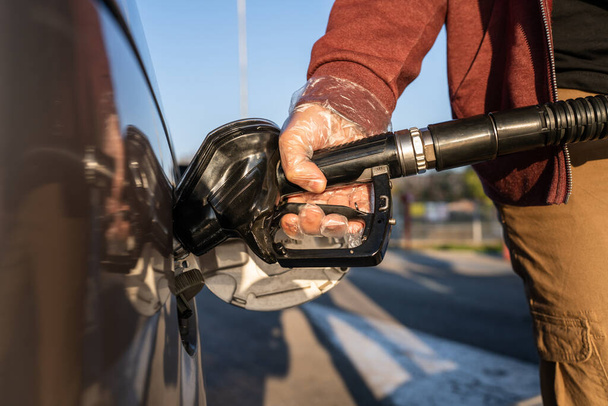 Close up on hand of unknown caucasian man hold black gas pump nozzle pouring gasoline into the fuel tank refueling petroleum to vehicle at self service petrol station during crisis copy space - Photo, Image