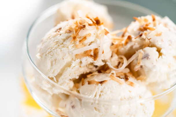 Homemade coconut ice cream garnished with roasted coconut flakes in a glass ice cream bowl. - 写真・画像