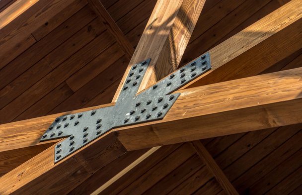 El conector de acero metálico asegura tres vigas de madera como parte de una estructura de techo. Conectores de construcción de madera diseñados para proporcionar soporte para aplicaciones en sistemas estructurales de madera - Foto, imagen