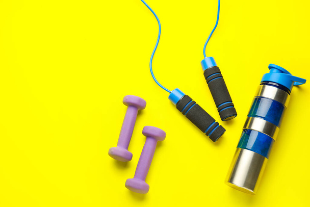 Dumbbells, skipping rope and bottle of water on yellow background - Photo, Image