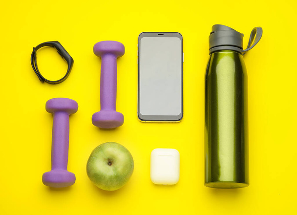 Dumbbells, gadgets and apple on yellow background - Photo, Image