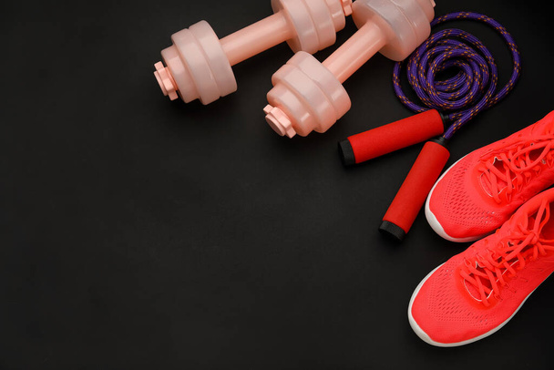 Dumbbells, shoes and skipping rope on dark background - Photo, Image