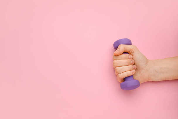 Female hand with dumbbell on pink background - Foto, Imagen