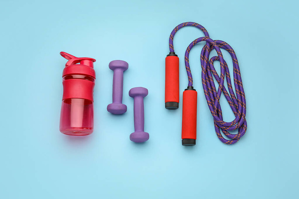 Dumbbells, bottle of water and skipping rope on blue background - Foto, afbeelding