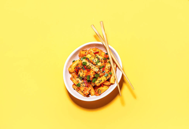 Bowl with honey chilli potato and chopsticks on color background - Photo, Image