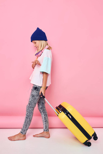 маленькая девочка в синих шляпах Желтый чемодан розовый фон - Фото, изображение