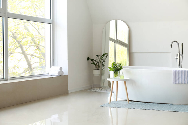 Interno della stanza luminosa con specchio e vasca da bagno - Foto, immagini
