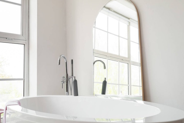 Σύγχρονη μπανιέρα και μεγάλο καθρέφτη στο φως δωμάτιο - Φωτογραφία, εικόνα