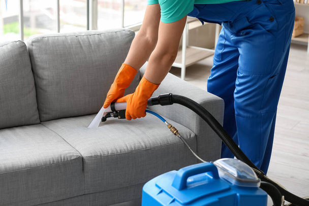Trabalhador masculino removendo mancha suja de sofá cinza com aspirador de pó no quarto - Foto, Imagem