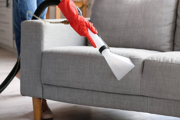 Mujer quitando la suciedad del sofá gris con aspiradora en casa - Foto, Imagen