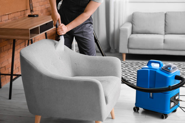 Male worker removing dirt from grey armchair with vacuum cleaner in room - Photo, Image