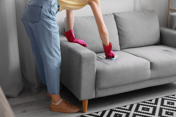 Woman cleaning grey sofa with sponge at home - Zdjęcie, obraz