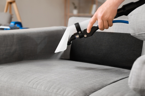 Conserje masculino quitando la suciedad del sofá gris con aspiradora en la habitación, primer plano - Foto, Imagen